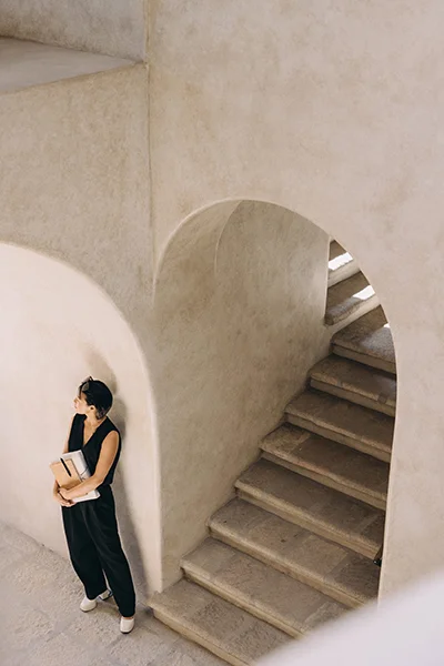 Professional woman holding a notebook and leaning against a stone wall beside a staircase